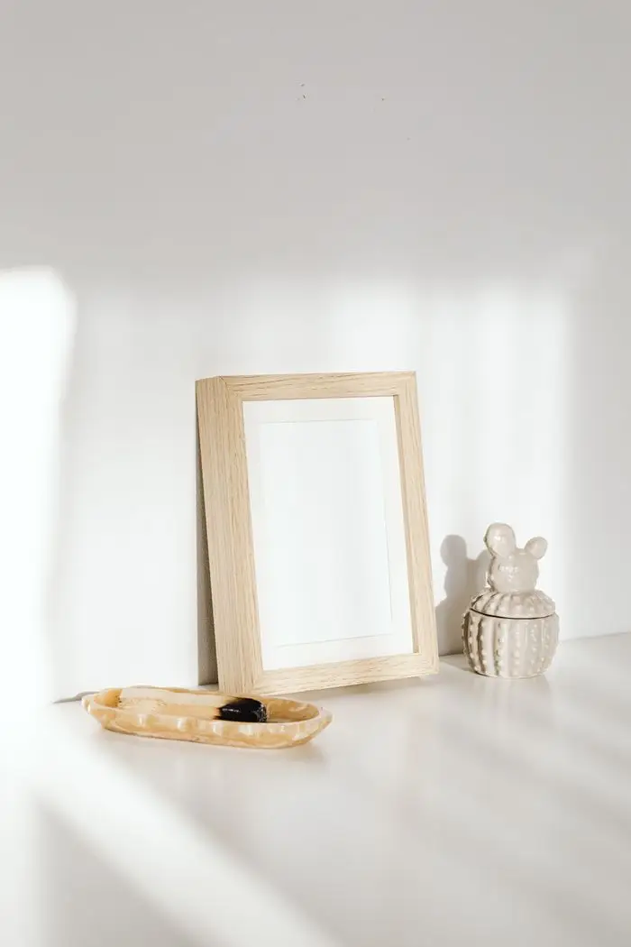 A wooden photo frame placed on a white tabletop with soft sunlight and shadows.